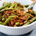 A serving bowl of green beans with plant based chorizo and shallots