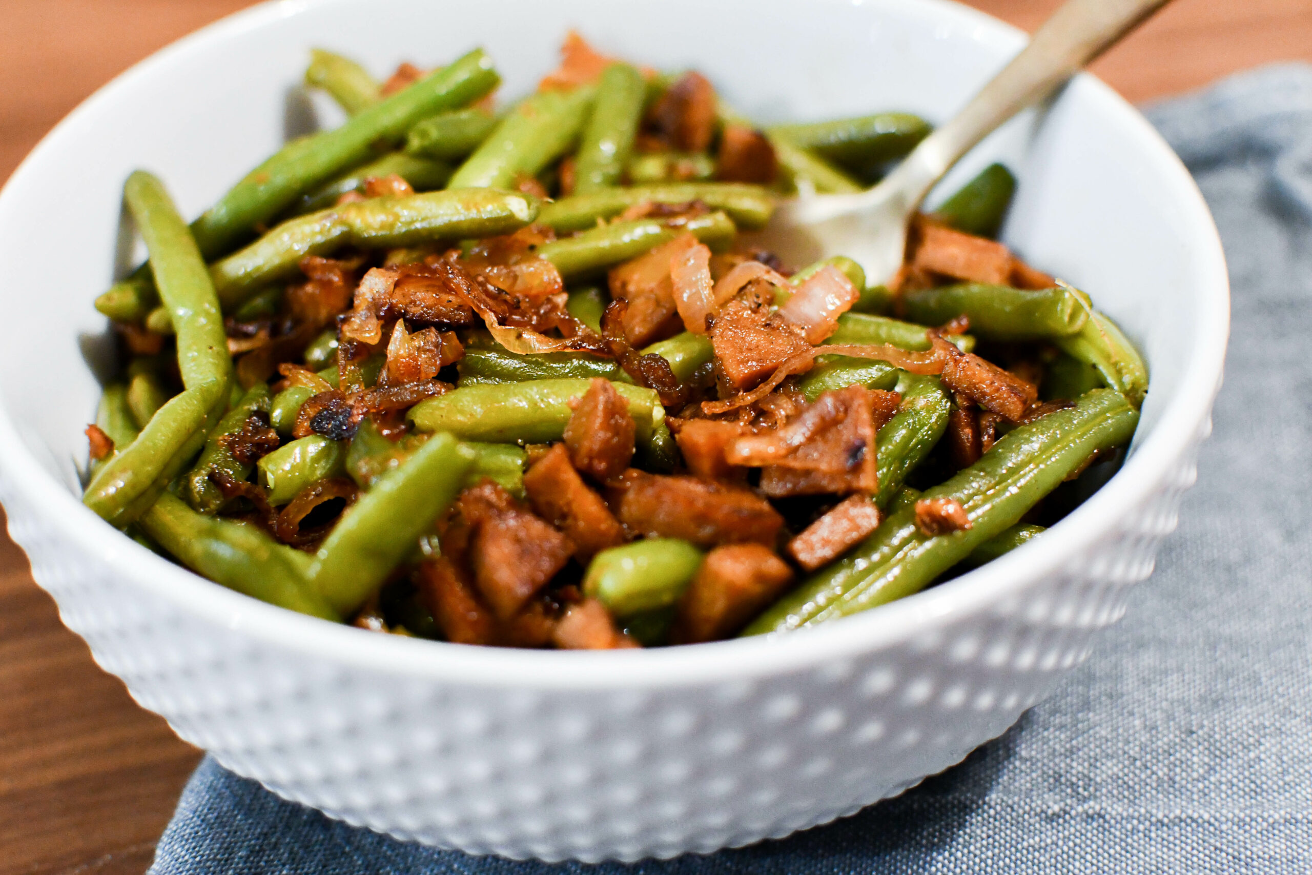 A serving bowl of green beans with plant based chorizo and shallots