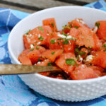 Photo of watermelon salad sitting on a picnic table with a blue napkin.